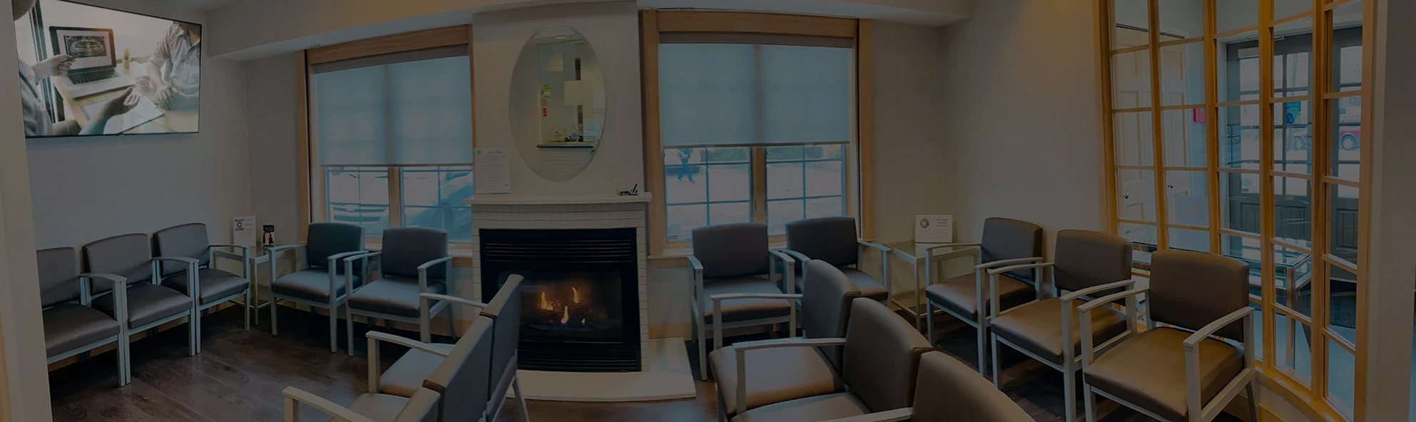 Modern dental office waiting room with seating, fireplace, large windows, and professional décor.