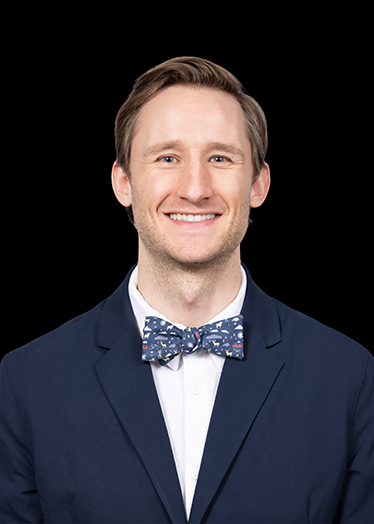 Professional headshot of smiling man in navy blazer and bow tie against black background.